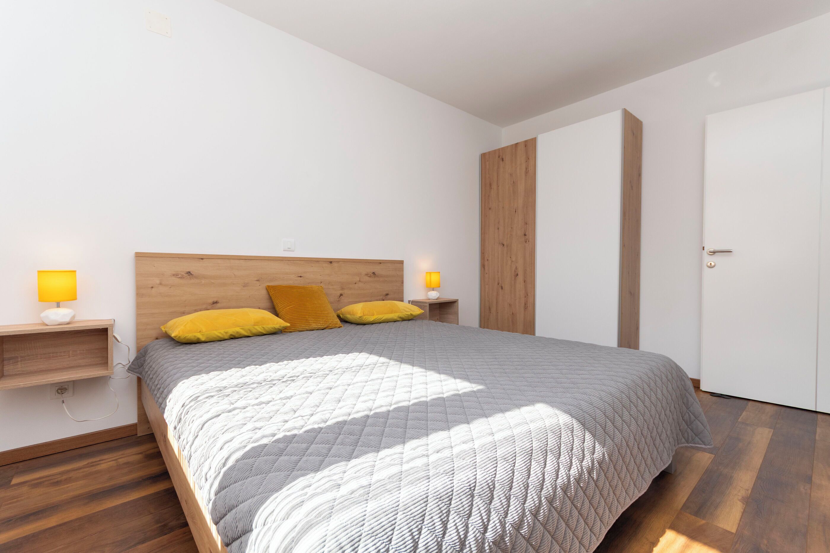 Une chambre à coucher comprenant un lit, des tables de chevet, une commode, une armoire en bois et une porte.