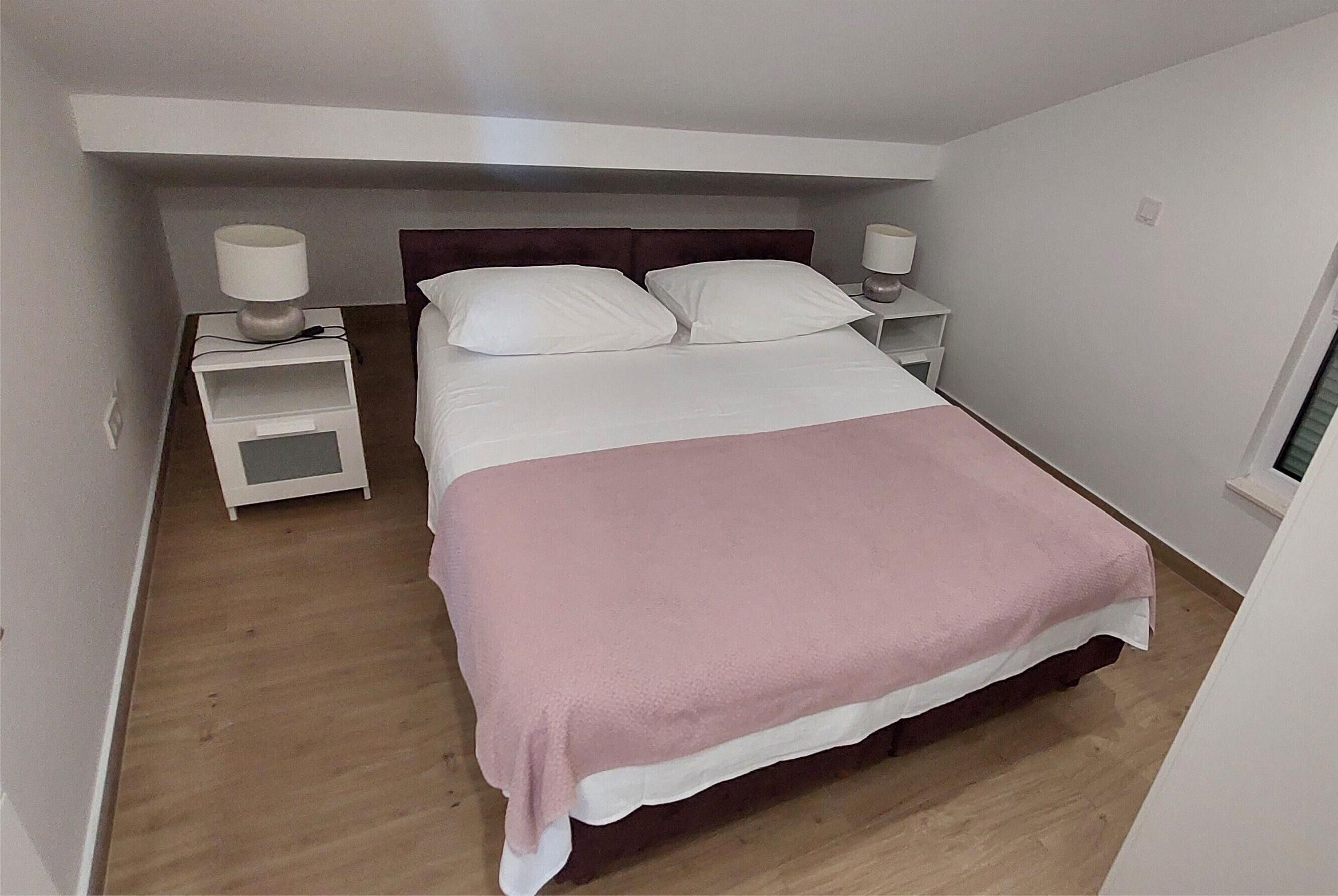 Ein kleines, ordentlich eingerichtetes Schlafzimmer mit einem Einzelbett, zwei Nachttischen und einem Fenster.