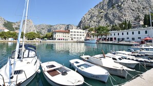 A marina with several boats docked, a rocky mountain in the background, and a white building with multiple windows. - Apartment Protrka (Omis)
