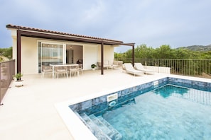A modern outdoor pool area with a covered patio, lounge chairs, and a view of the surrounding landscape. - House Vrsinka (Marina)