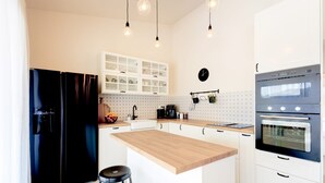 A modern kitchen with a central island, black refrigerator, white cabinets, and a double oven. - House Vrsinka (Marina)