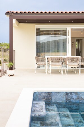 A modern outdoor patio with a pool, white wicker furniture, and a glass door leading to a covered area. - House Vrsinka (Marina)