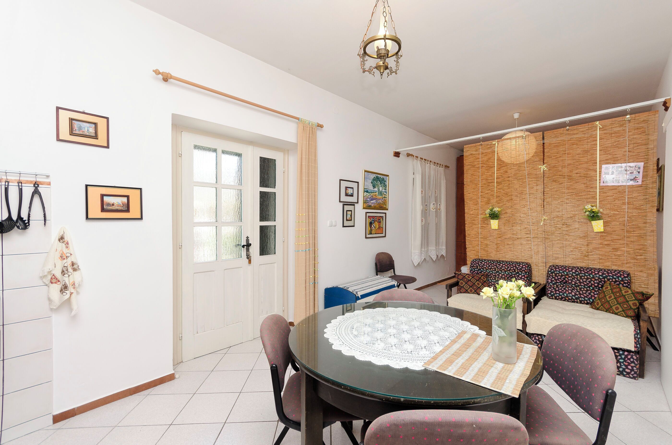 Un coin repas comprenant une table ronde en verre, des chaises, un vase avec des fleurs, un canapé et un mur décoré de tableaux.