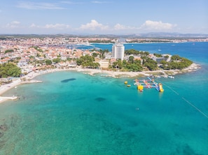 An aerial view of a coastal town with a marina, clear turquoise waters, and a prominent white building. - Apartment Vintage Dalmatia Stay (Vodice)