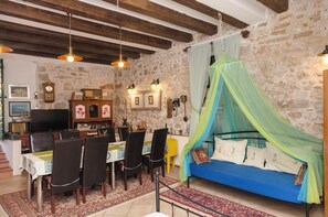 A rustic room with a stone wall, a bed with a canopy, a dining table with chairs, a television, and a clock. - Apartment Vintage Dalmatia Stay (Vodice)