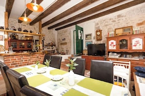 A rustic dining area with a brick wall, wooden beams, a green door, and a television. - Apartment Vintage Dalmatia Stay (Vodice)