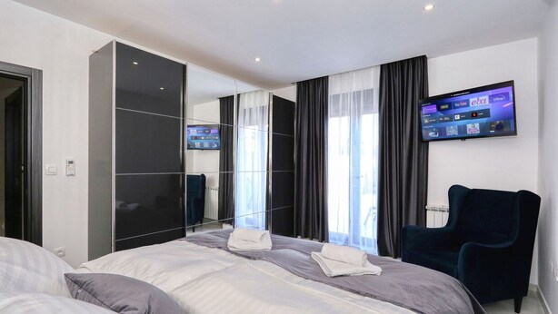 A hotel room with a bed, a TV mounted on the wall, and a chair. - Apartment Viktor (Zadar)