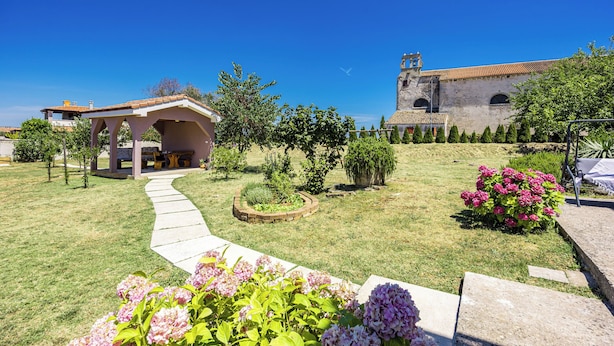 A courtyard with a stone pathway, a pergola, and a building with a bell tower. - Apartment Gradina (Vodnjan)