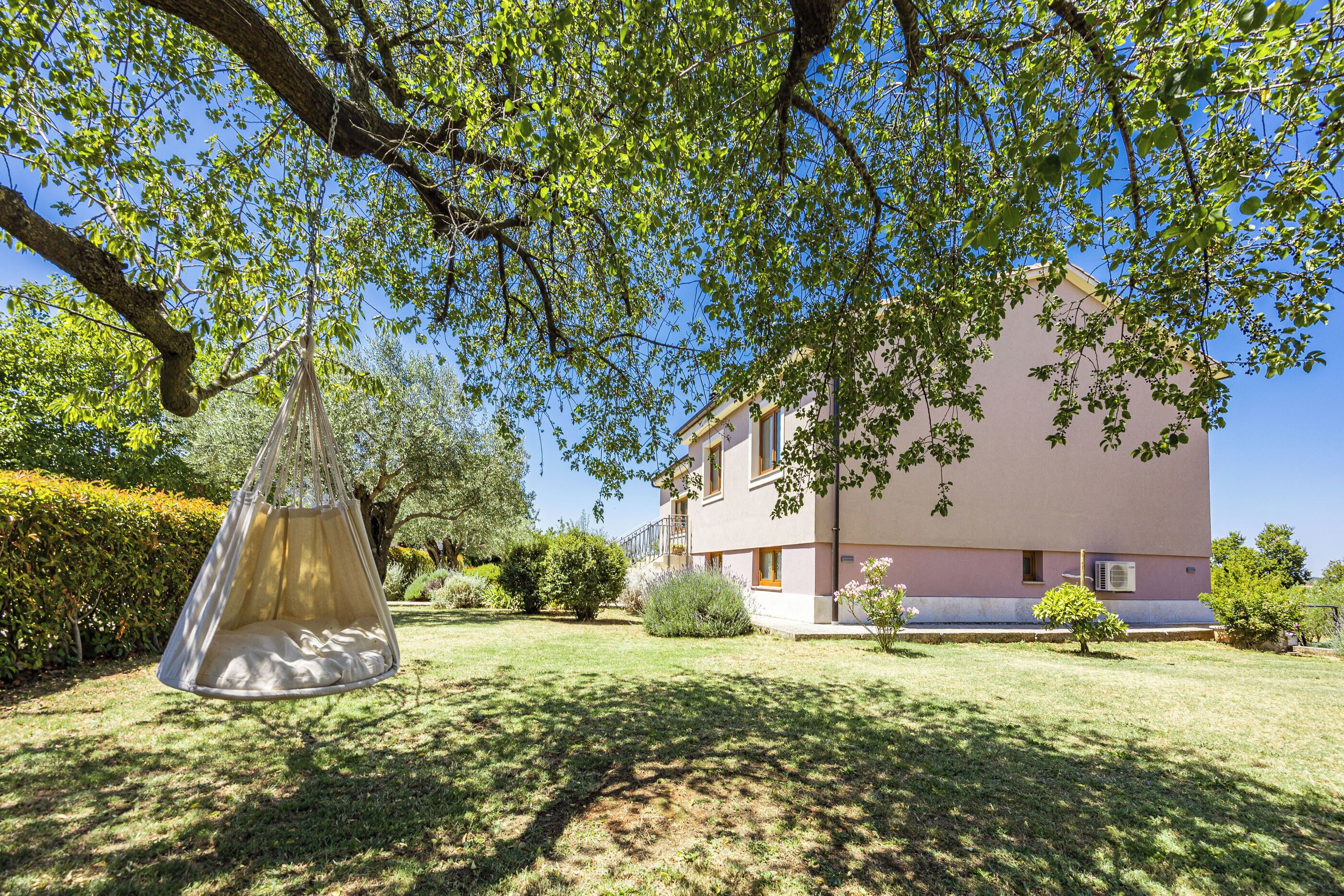 A garden with a hanging chair, a building with a pink facade, and a clear blue sky.