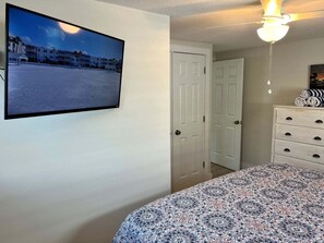 Ein Schlafzimmer mit einem Bett, einer Kommode, einem an der Wand befestigten Fernseher und einer Tür zu einem anderen Raum.