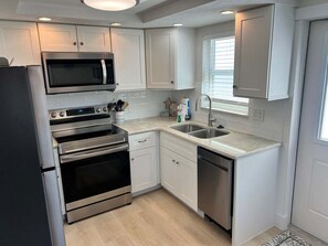 A modern kitchen with stainless steel appliances, white cabinetry, and a window providing natural light. - Casa Blanca - Villa D12 (Sarasota)