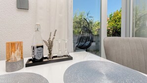 A modern living room with a white textured wall, a black thermostat, a glass table with decorative items, and a view of greenery outside. - Apartments Sunny (Vodice)