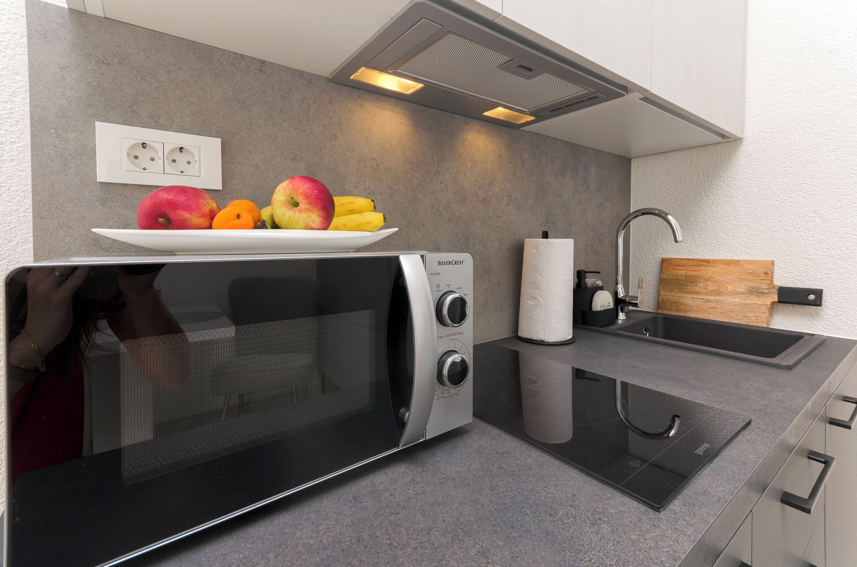 A modern kitchen with a built-in microwave, a sink, and a countertop with fruits.
