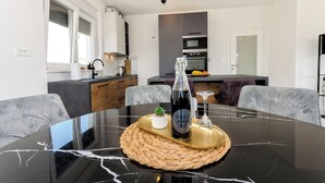 A modern kitchen with white cabinets, a black countertop, and a dining table with a marble top. - Apartments Sunny (Vodice)
