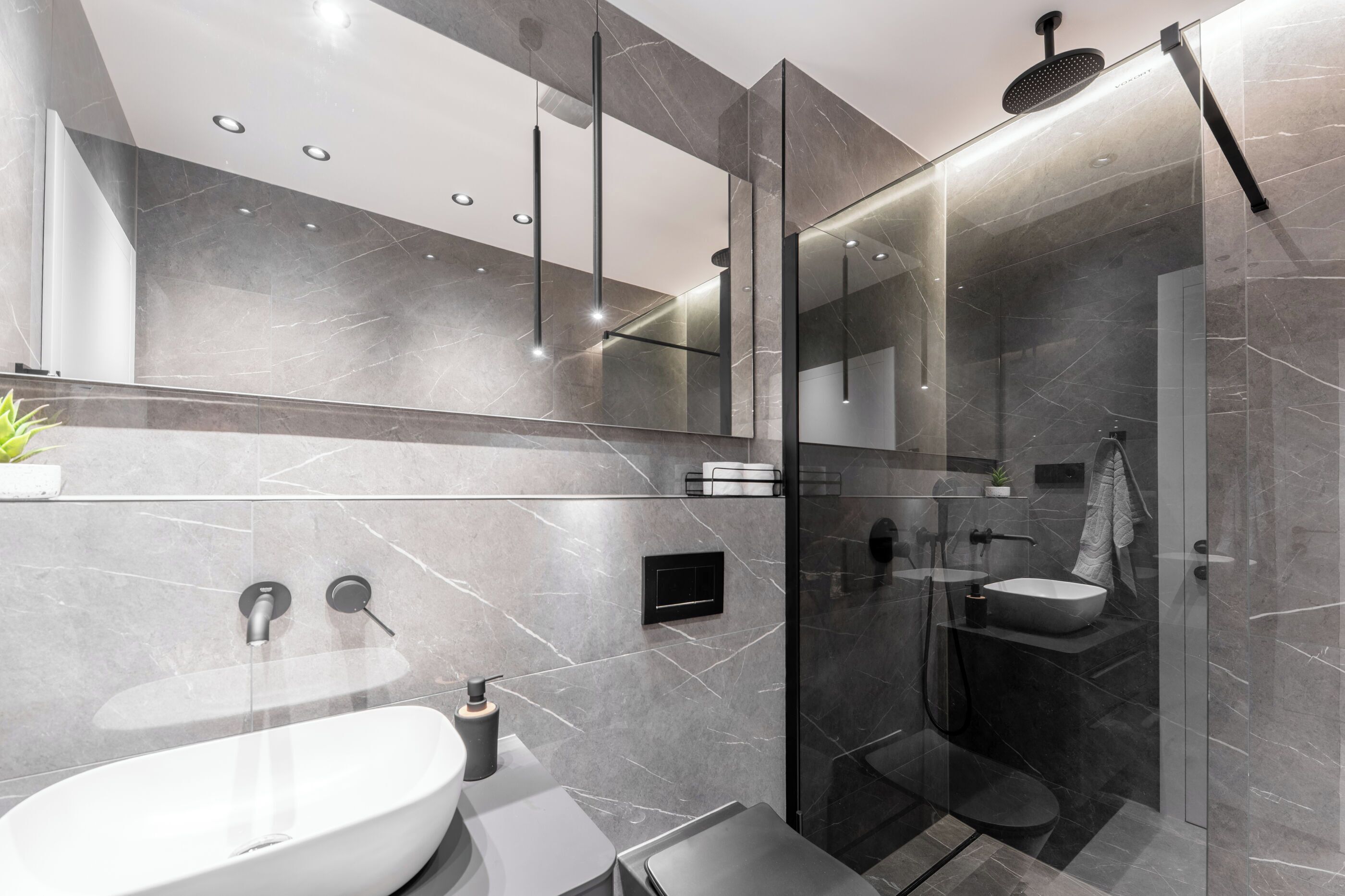 A modern bathroom with a large white sink, a glass-enclosed shower, and a marble-tiled wall.