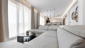 A modern living room with a large L-shaped sofa, a round black coffee table, and a kitchen in the background. - Apartment Luka (Baska Voda)