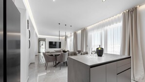 A modern kitchen with a central island, dining area with chairs, and large windows with curtains. - Apartment Luka (Baska Voda)