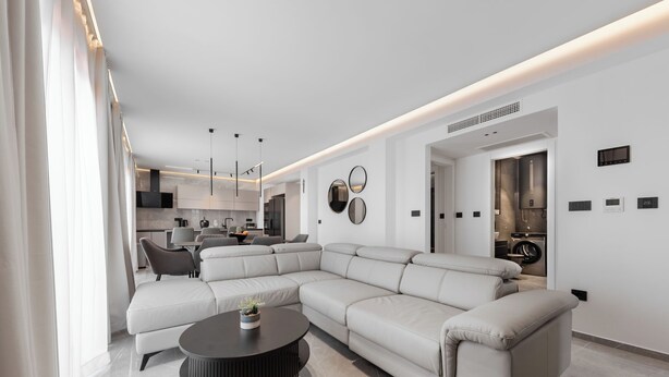A modern living room with a sectional sofa, a round coffee table, and a kitchen in the background. - Apartment Luka (Baska Voda)
