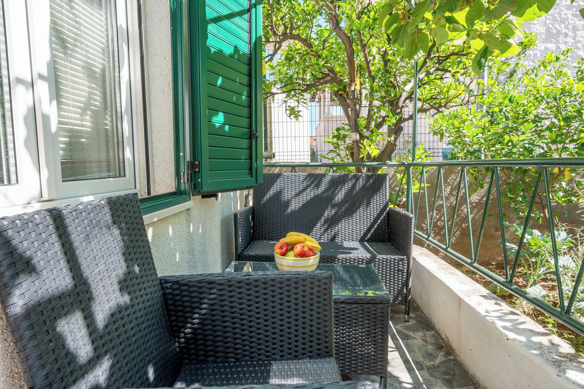 Un balcón con mobiliario de mimbre, una mesa de vidrio y un frutero.