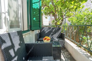 Ein Balkon mit Korbmöbeln, einem Glastisch und einer Obstschale.