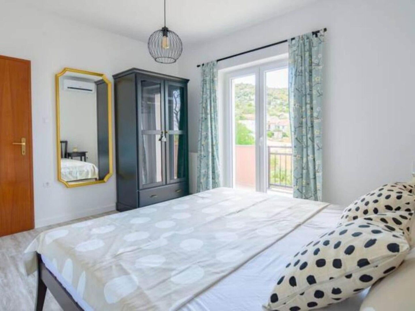 A bedroom with a bed, a wardrobe, a mirror, and a balcony with curtains.