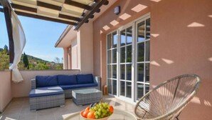 Un espace extérieur aménagé en terrasse, avec un canapé, une table ronde sur laquelle est posé un panier de fruits et une chaise en osier.