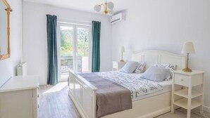 Une chambre à coucher avec un lit, des tables de chevet, un miroir et une fenêtre avec des rideaux.