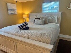 Quarto com cama, almofadas, abajur e janela com persianas.