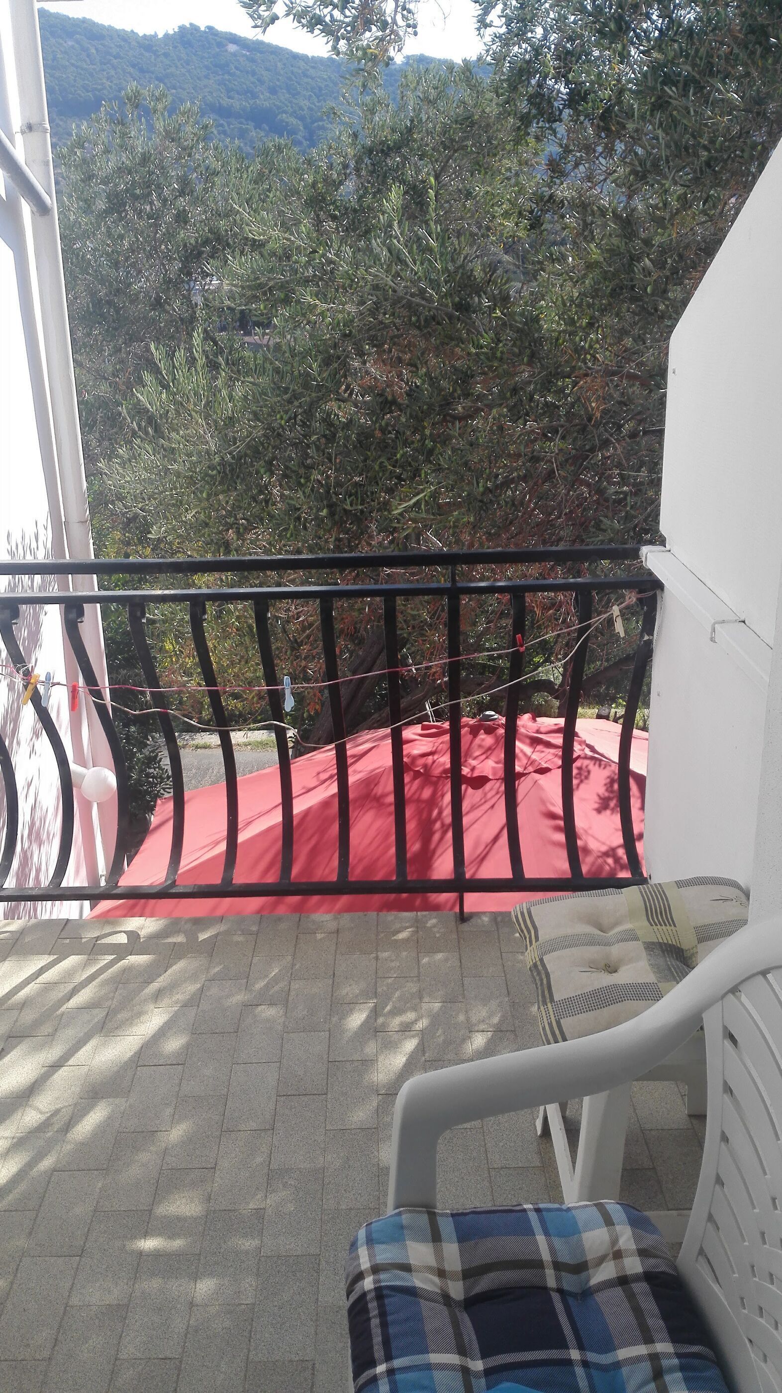 A balcony with a red cloth, a white chair, and a metal railing.