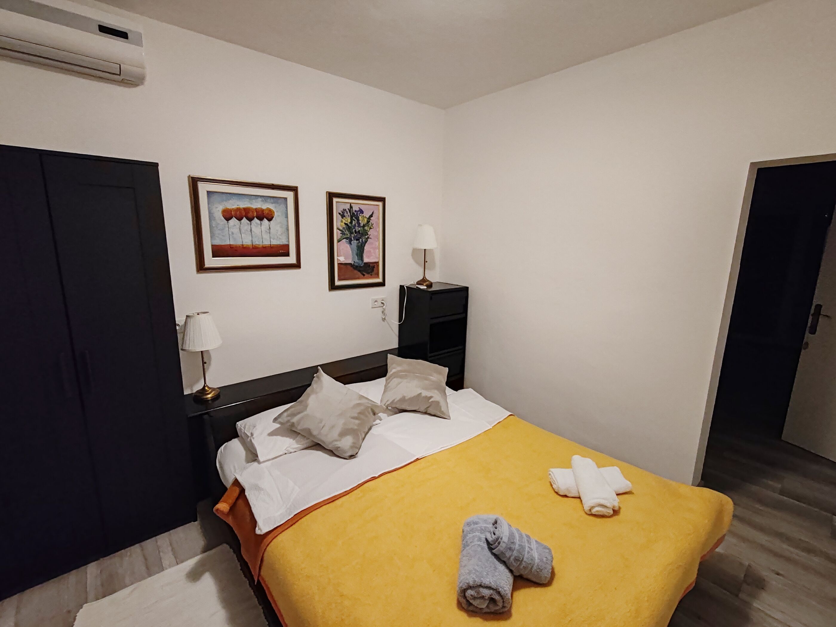 Ein Hotelzimmer mit einem Bett, einem Nachttisch, einer Lampe und zwei gerahmten Bildern an der Wand.