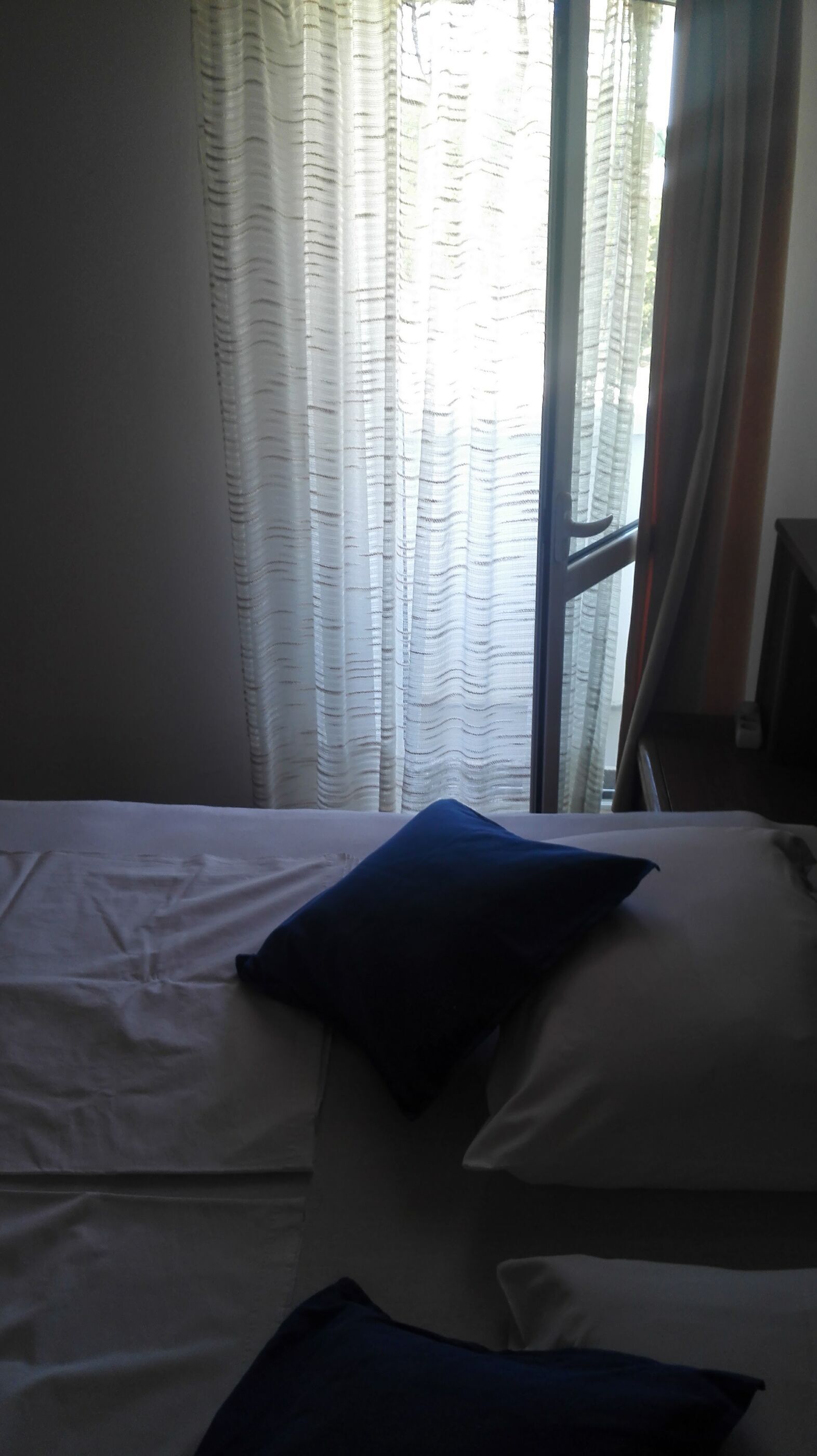 A room with a bed, white curtains, and a window with a view of trees.