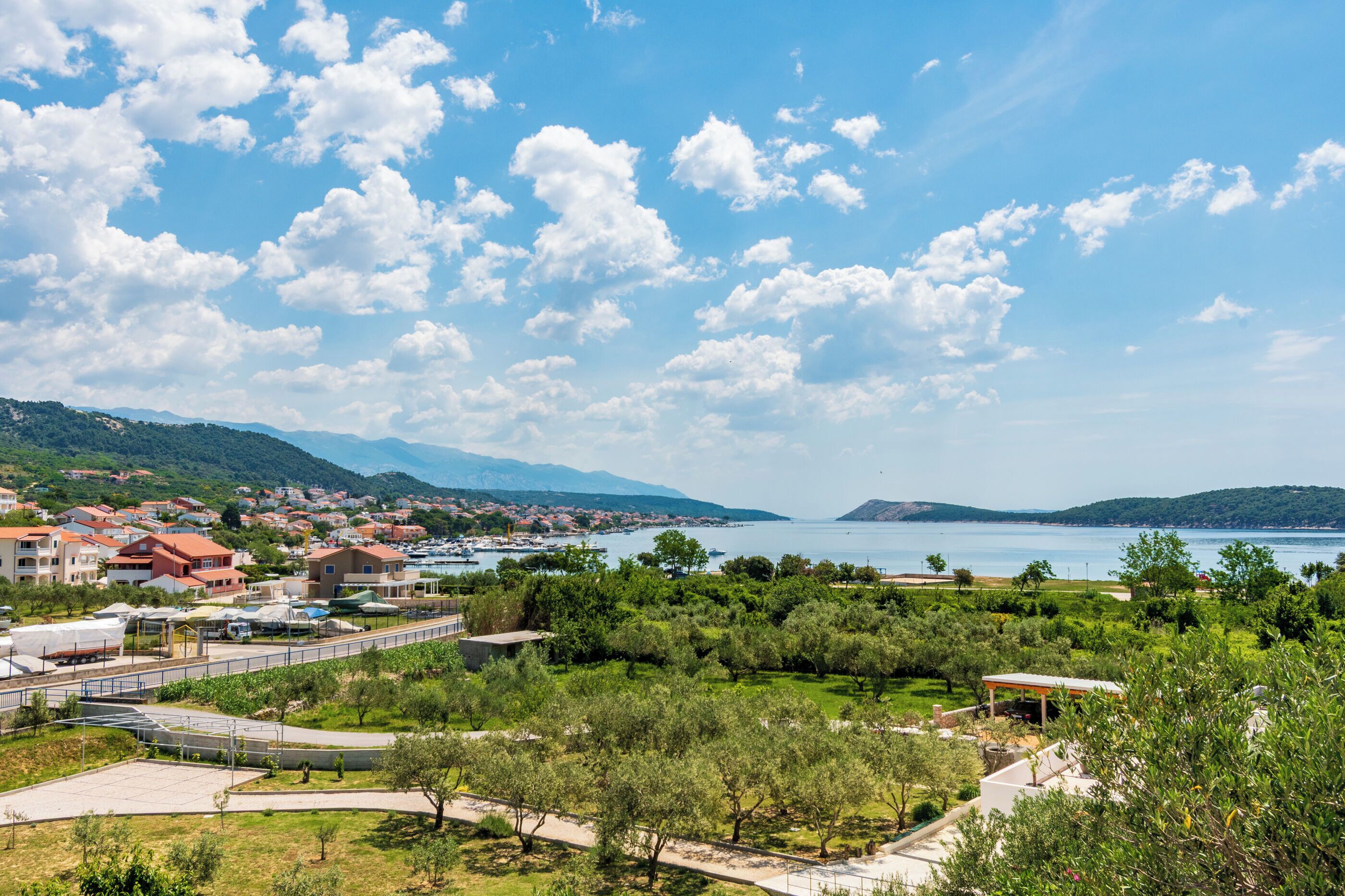 Une ville côtière dotée d’un port de plaisance, de collines verdoyantes et d’un ciel dégagé.