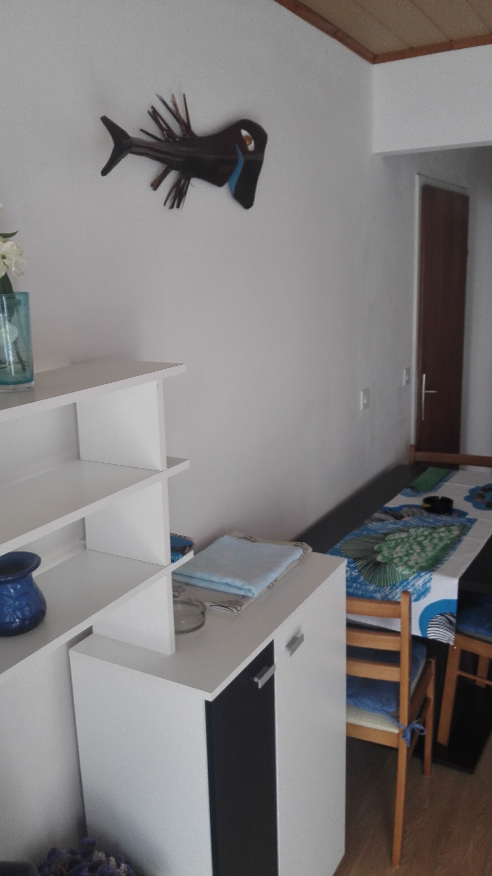 Cocina compacta con muebles blancos, un refrigerador pequeño y un comedor con mesa y sillas.