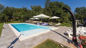 A rectangular swimming pool with a tiled deck, surrounded by lounge chairs and umbrellas. - Apartments Cetri Hrasta (Pican)