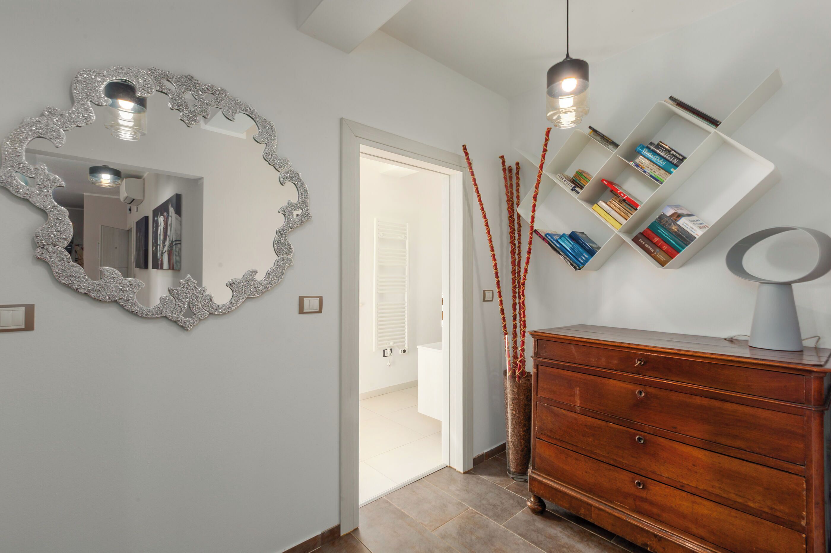 A hallway with a mirror, a wooden dresser, and a bookshelf.