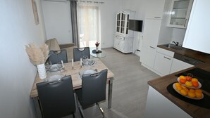 A modern kitchen with white cabinets, a dining area with a wooden table and chairs, and a fruit display on the counter. - Apartment Milankovic (Vrsar)