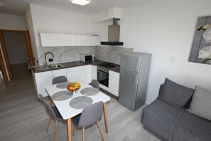 A compact kitchen with a dining table, chairs, a refrigerator, a microwave, and a stove. - Apartment Milankovic (Vrsar)