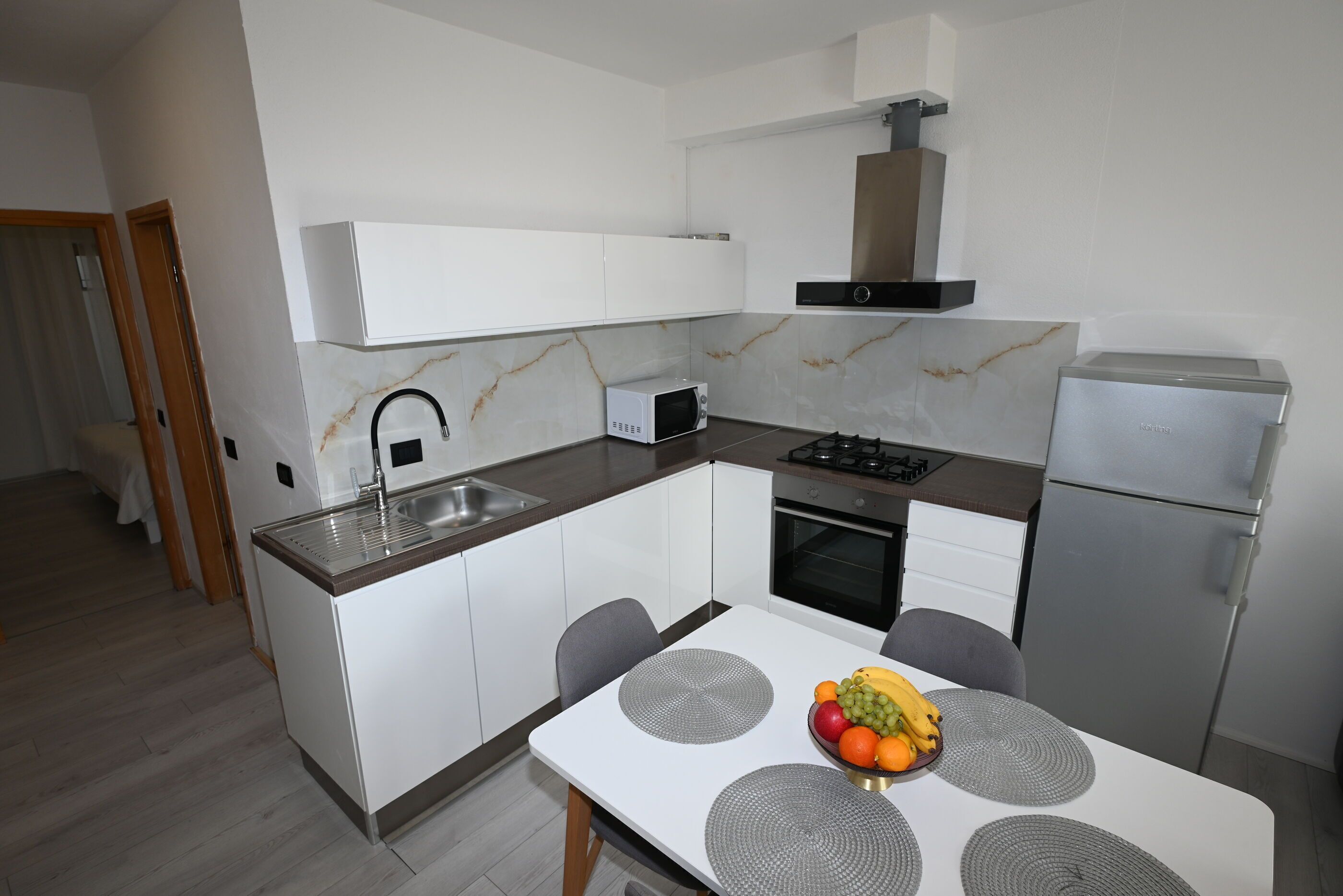 A modern kitchen with white cabinets, a stainless steel sink, a microwave, a gas stove, and a refrigerator.