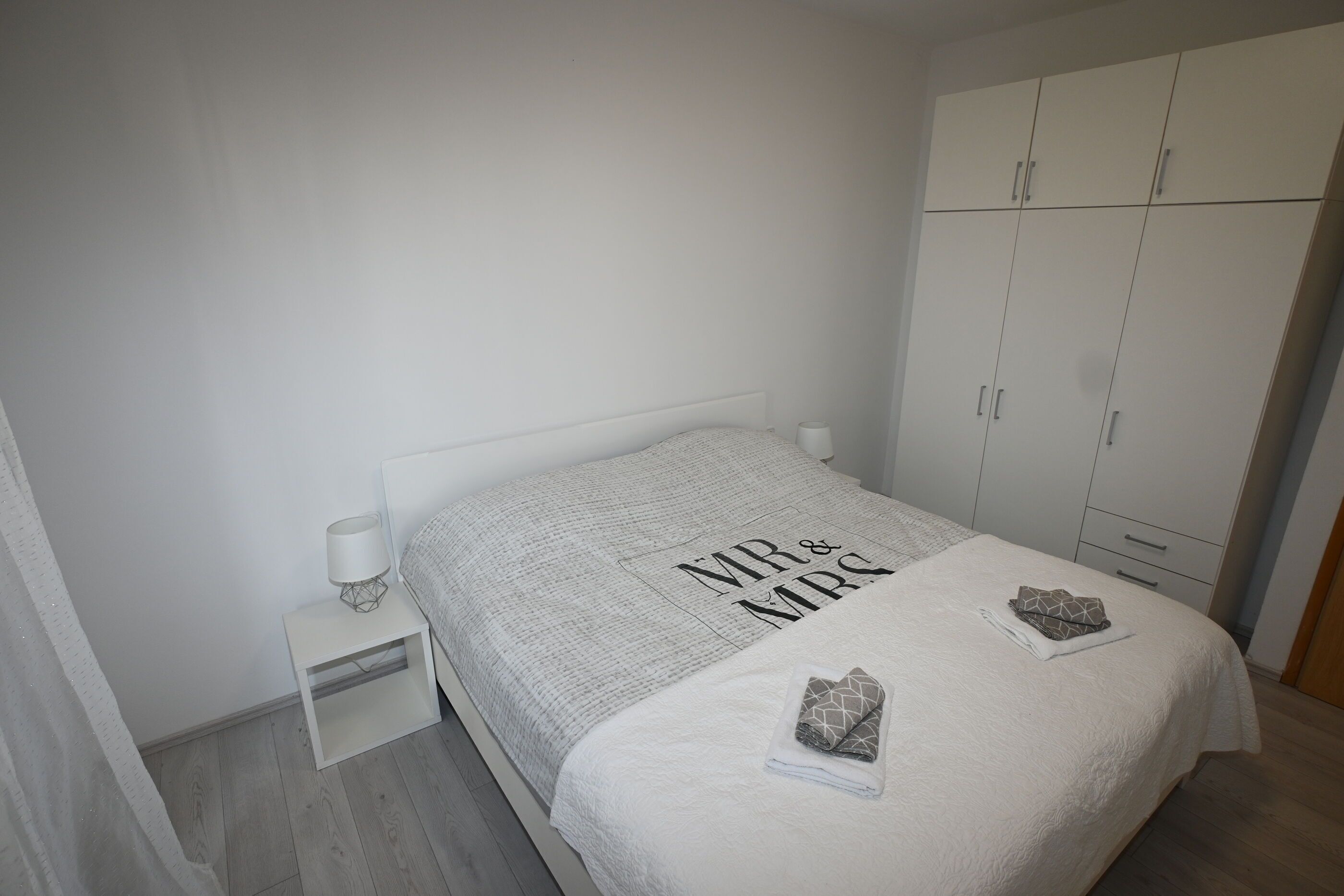A bedroom with a bed, a nightstand, a wardrobe, and a curtain.