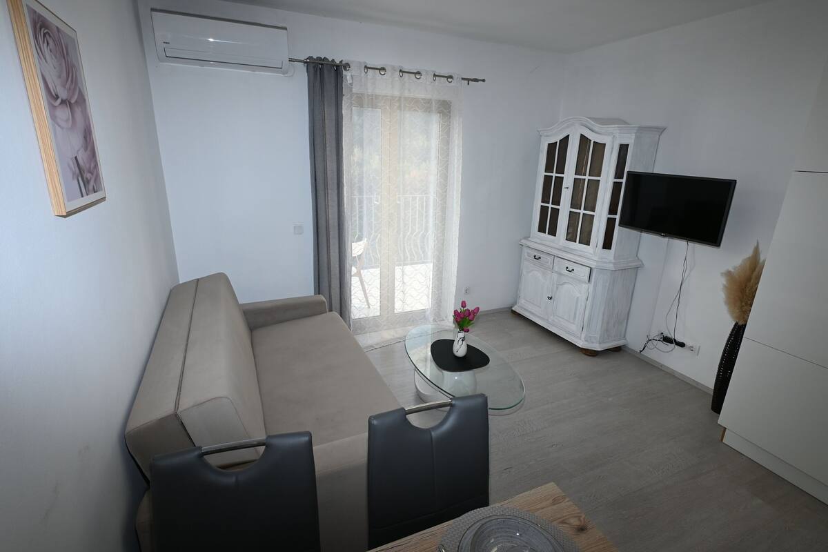 A modern living room with a beige sofa, a glass coffee table, and a white cabinet with a TV mounted above it.