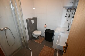 Une petite salle de bain avec une douche à parois de verre, des toilettes, une poubelle noire et une baignoire blanche.