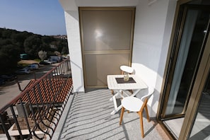Un balcon avec une table et des chaises, une porte et une vue sur les voitures garées et les arbres.