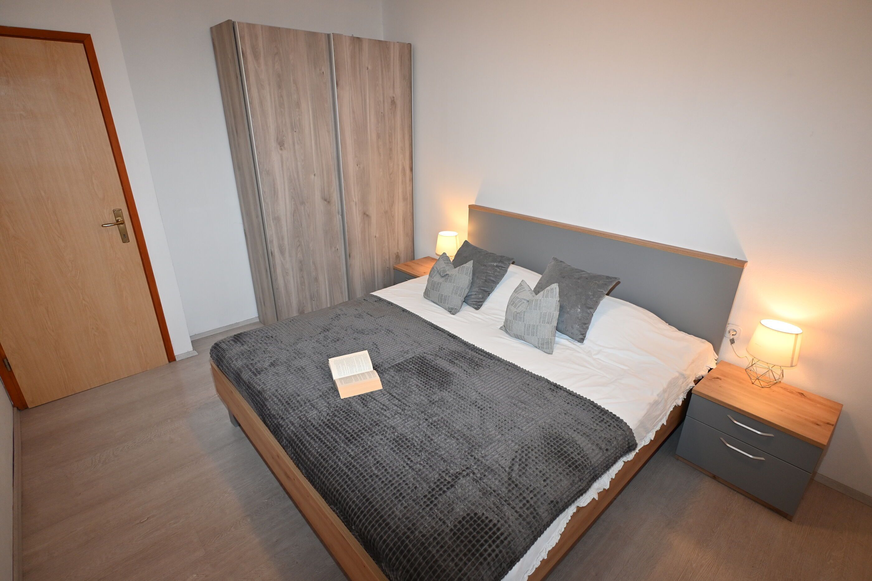 Un dormitorio con cama, mesitas de noche, armario y una puerta.