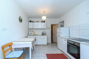 A compact kitchen with a microwave, coffee maker, and oven. There is a dining table with a chair, and a refrigerator in the background. - House Toni (Rab)