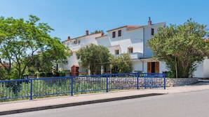 A row of white buildings with red roofs, a blue fence, and trees in front. - House Toni (Rab)