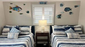 Ein Schlafzimmer mit zwei Betten, einem Nachttisch, einer Lampe und Wanddekorationen, darunter Fische.