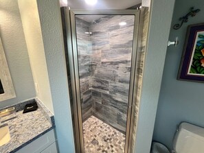 Un baño con cabina de ducha de vidrio, encimera de mármol y suelo de baldosas.