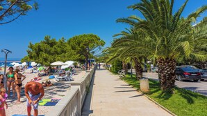 A beachside walkway with palm trees, beach umbrellas, and people. - Room Laura (Crikvenica)