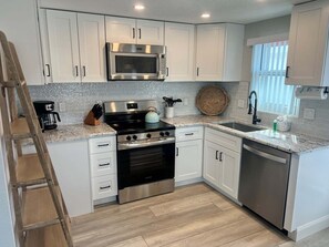 A modern kitchen with white cabinets, stainless steel appliances, and a wooden floor. - Casa Blanca - Villa D02 (Siesta Key)