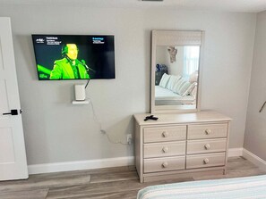 Ein Schlafzimmer mit einem an der Wand befestigten Fernseher, einer Kommode mit Schubladen und einem Bett mit gestreifter Bettdecke.